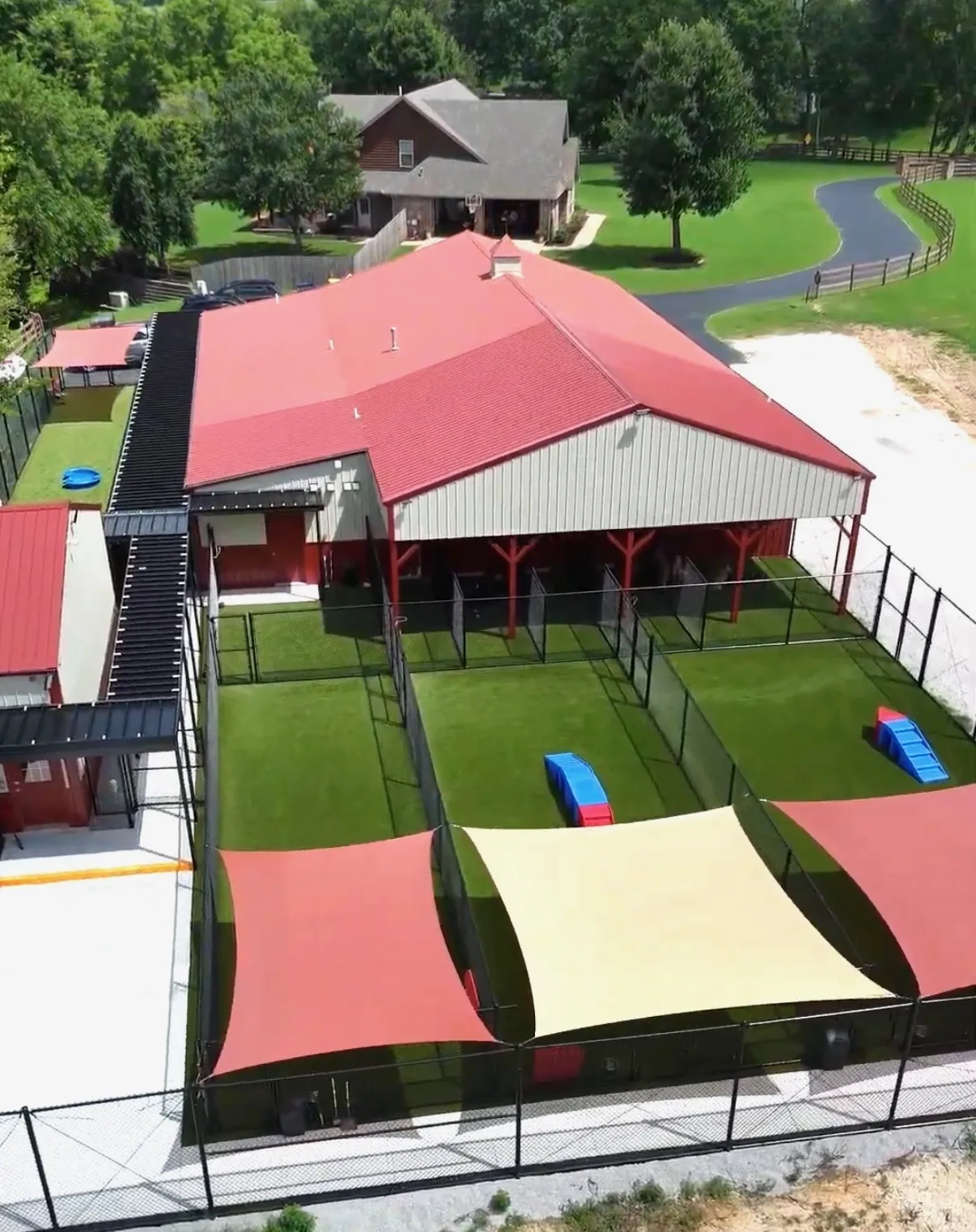 Aerial view of the Canine Nation facility in Farmington, Arkansas — covered kennel runs, shaded turf play yards, and the training center